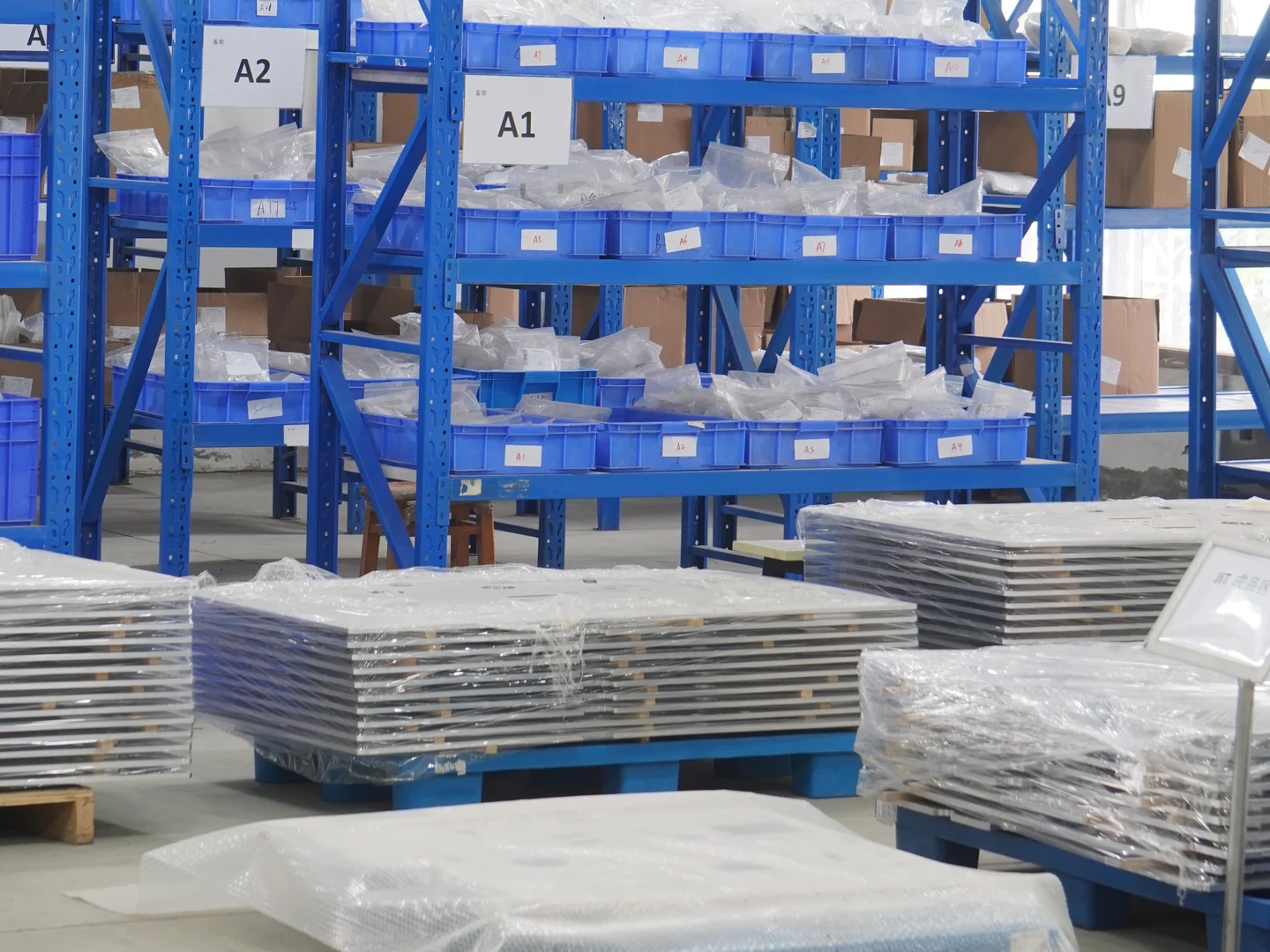Wrapped machined parts on pallets beside workshop storage racks